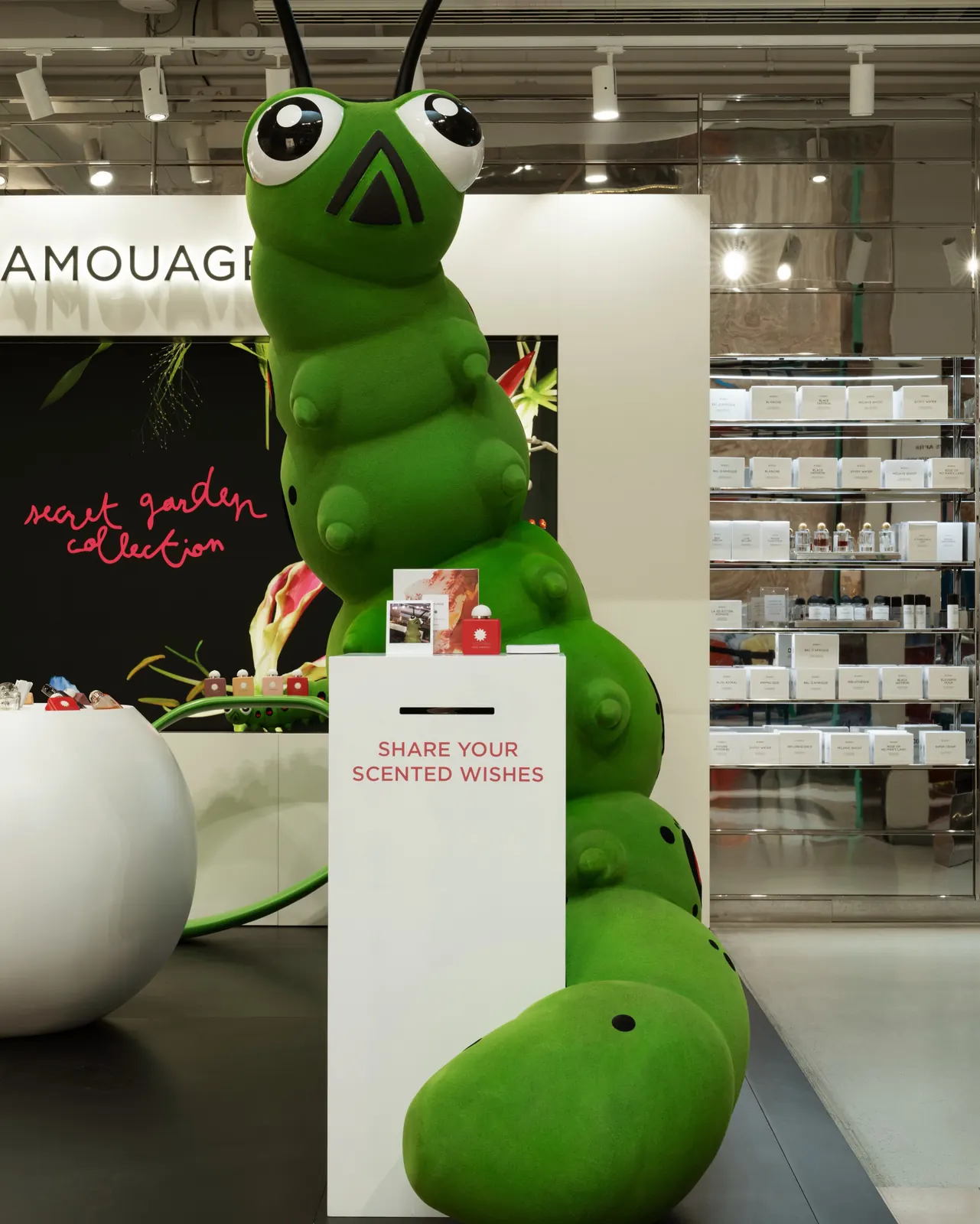 Carter the caterpillar mascot amid hibiscus-themed display at Amouage Paris pop-up