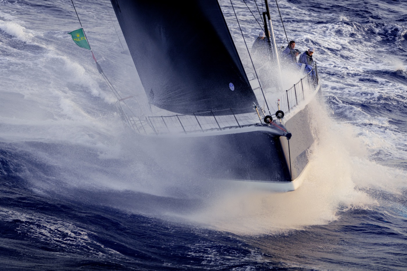 A maxi yacht under the Rolex flag driving through spray in the central Mediterranean